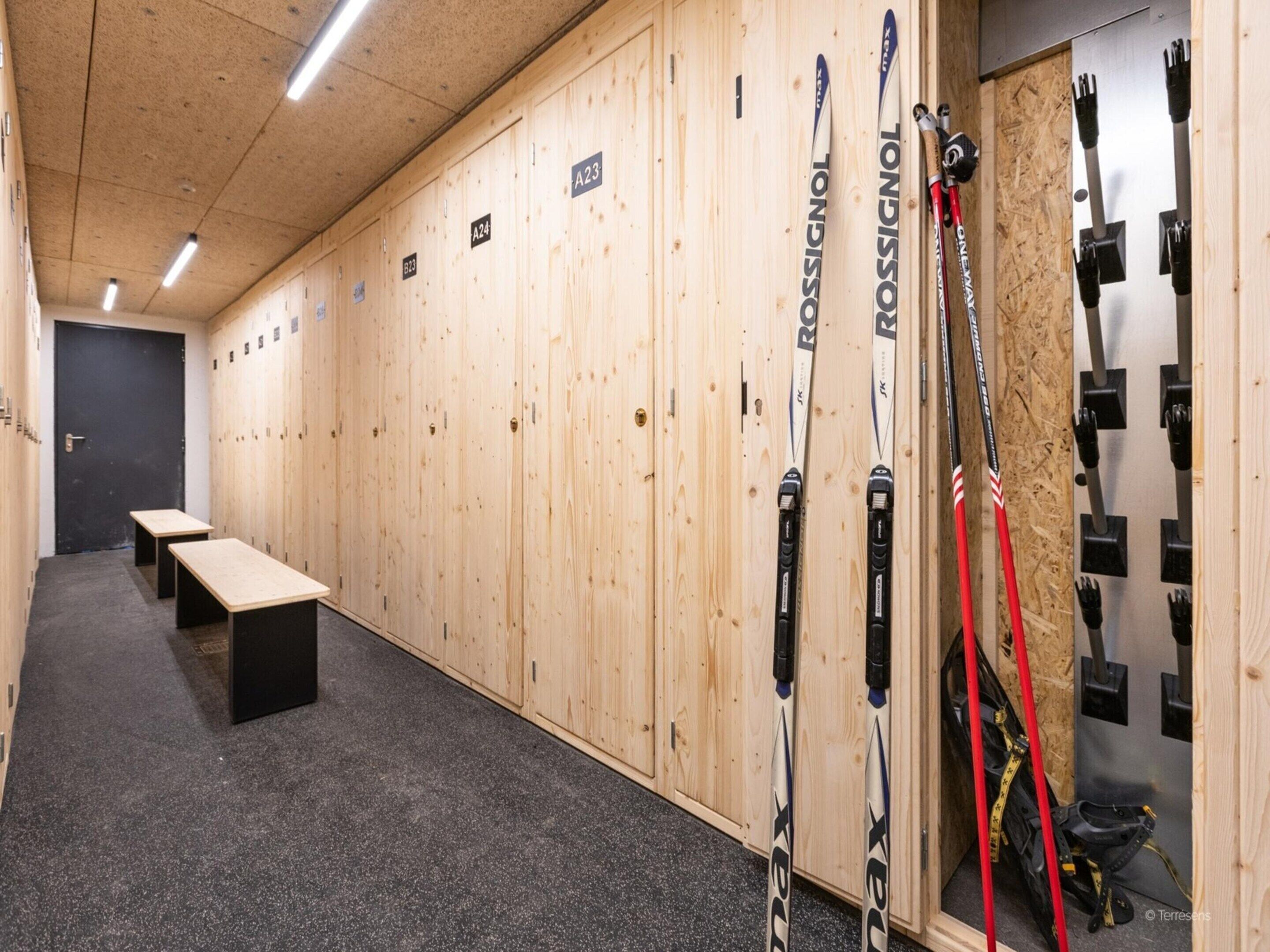 A locker room with wooden lockers, benches, and skis.