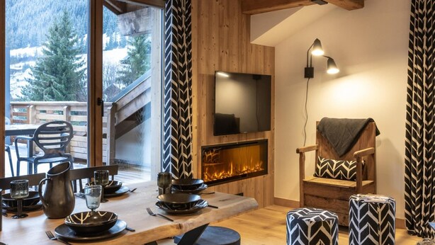 Una sala de estar acogedora con chimenea, vigas de madera y un amplio ventanal con vistas a un paisaje nevado.