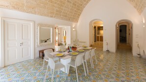 Un coin repas avec une table dressée pour quatre personnes, des chaises blanches, un sol à motifs et un plafond en pierre.