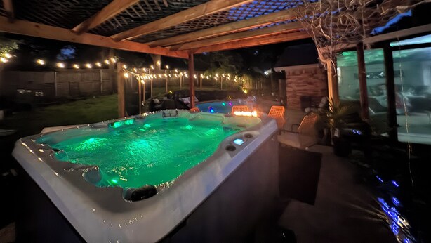 A hot tub with a wooden pergola overhead, surrounded by outdoor seating and string lights. - 6mi from AT&T-HEATED POOL-HOT TUB-INDOOR BAR-TOP KITCHEN AMENITIES-SLEEPS 12+ (Arlington)