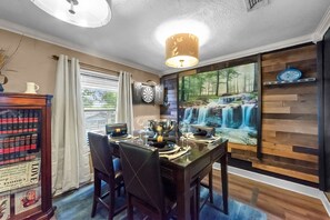 Een eetruimte met een houten tafel gedekt voor vier personen, een kroonluchter en een muurschildering van een waterval.