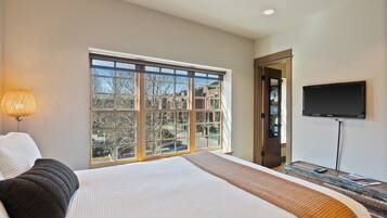 A hotel room with a large bed, a TV mounted on the wall, and a window with a view of buildings.