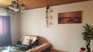 En stue med en sort lædersofa, et glasbord, træloft, en lysekrone, et billede på væggen og en potteplante med røde roser.