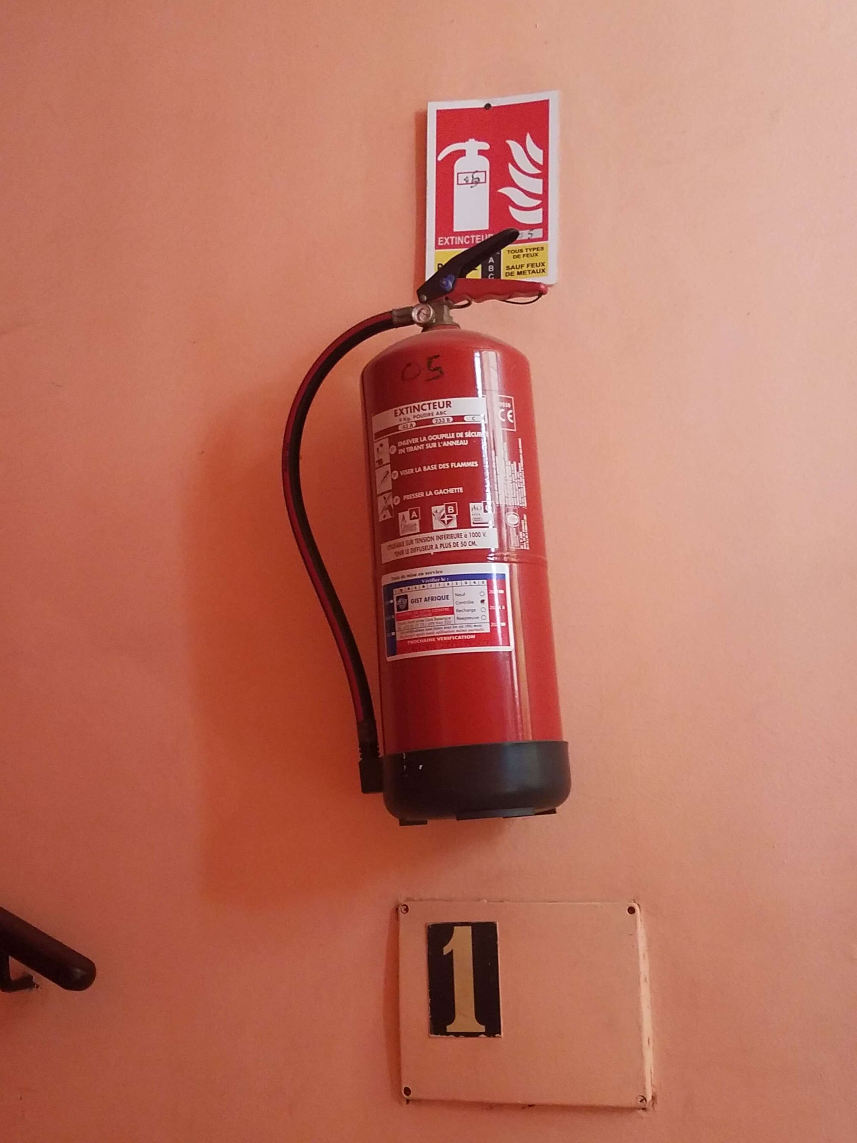 Extintor rojo montado en la pared, con un cartel de seguridad contra incendios encima y una placa numerada debajo.