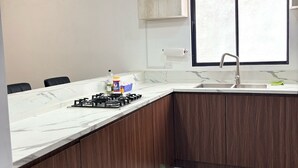 Une cuisine moderne dotée d’un plan de travail en marbre, de meubles en bois, d’une cuisinière à gaz et de luminaires suspendus.