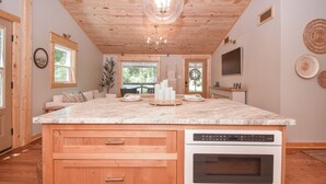 Una cocina con armarios de madera, una isla grande con horno integrado y una lámpara colgante.