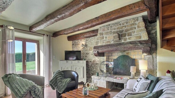 A rustic room with exposed wooden beams, a stone fireplace, a television, a comfortable sofa, and a dining table. - Des Puits - LOCOAL-MENDON (LOCOAL-MENDON)