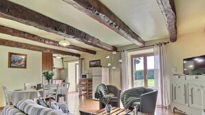 A spacious living area with exposed wooden beams, a dining table, a sofa, and a television on a cabinet. - Des Puits - LOCOAL-MENDON (LOCOAL-MENDON)