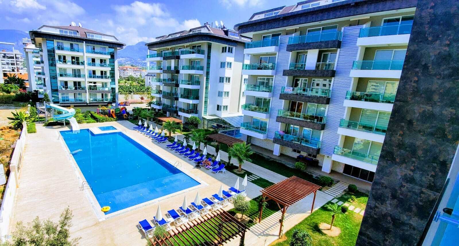 A modern hotel with multiple floors, a swimming pool, and outdoor seating areas.