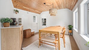 A modern kitchen with wooden cabinets, a dining table, and a hanging light fixture. - Remodeled 2-bedroom house with hot tub, 7mins to Saugatuck & beach (Fennville)