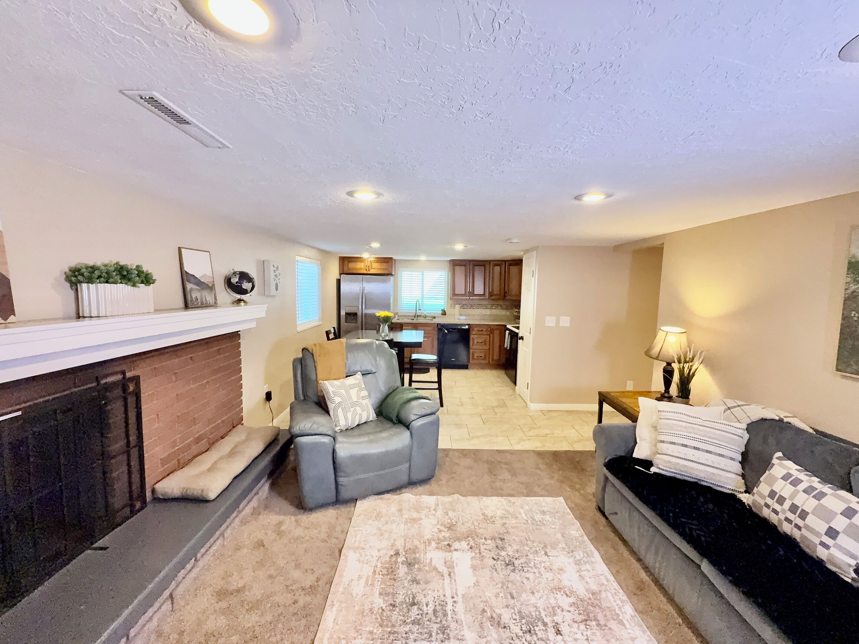 A living room with a fireplace, a sofa, a coffee table, and a kitchen in the background.