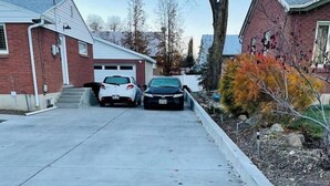 Eine Auffahrt mit zwei geparkten Autos, einer Garage und einem Haus mit Ziegelverkleidung.