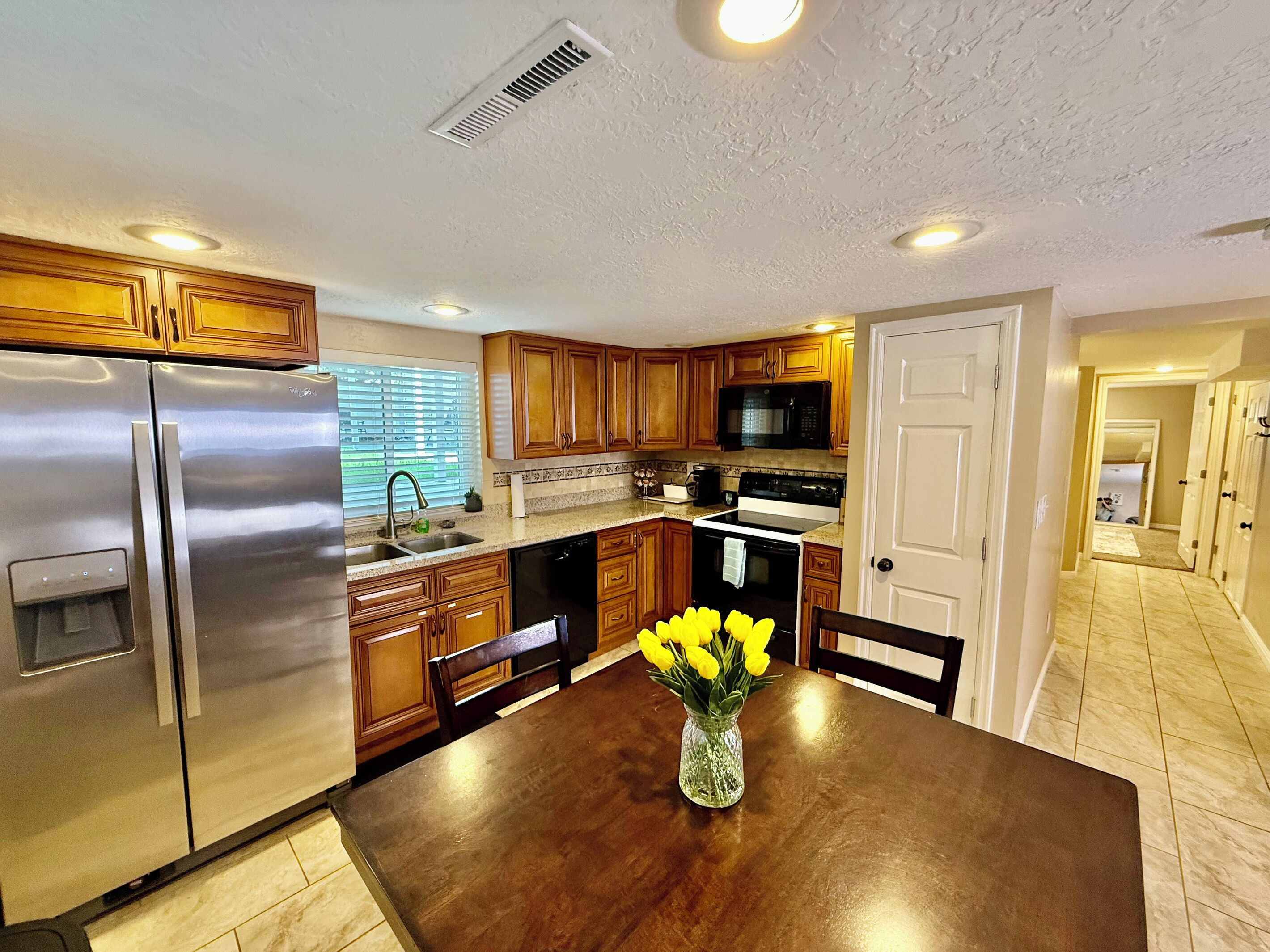A modern kitchen with stainless steel appliances, wooden cabinets, and a dining table with a vase of flowers.
