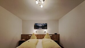 A modern bedroom with a large bed, wooden headboard, bedside tables, and a wall-mounted picture.