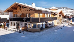 Un grand chalet à plusieurs étages, doté d’une façade en bois, d’un balcon et d’une piste de ski en arrière-plan.