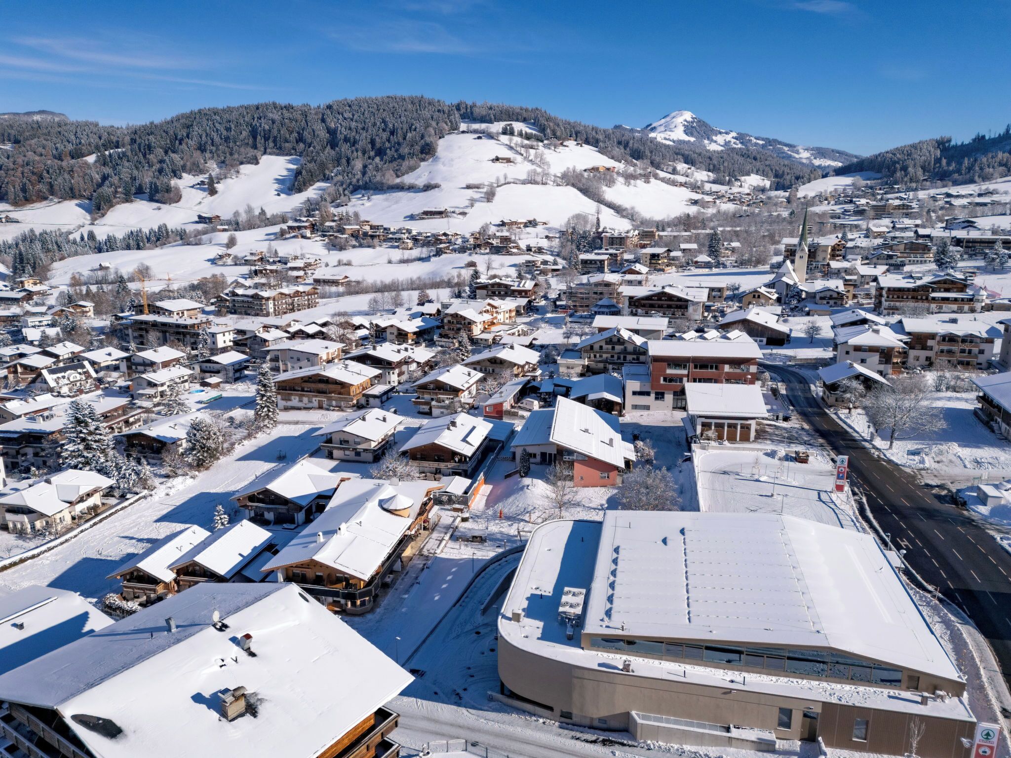 A snow-covered village with traditional wooden houses and a modern building with a curved roof.
