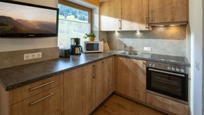 A modern kitchen with wooden cabinets, a built-in oven, a microwave, and a coffee maker. - Daniela by Interhome (Niederau)