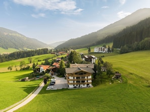 A rural mountain village with a prominent hotel featuring a balcony and a parking area.