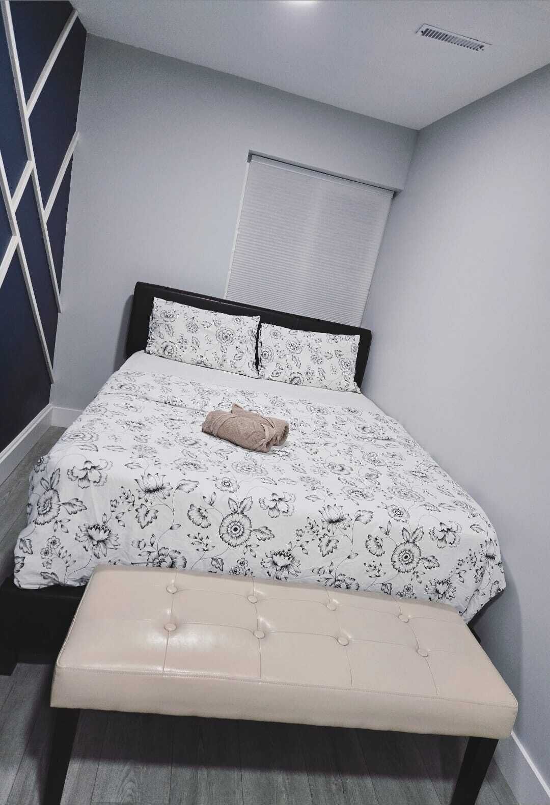 A bedroom with a bed, a bench, a window with blinds, and a geometric wall design.