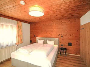 A bedroom with a wooden ceiling, a bed with white bedding, a small bedside table, and a window with curtains. - Apartment Manuel by Interhome (Hippach)