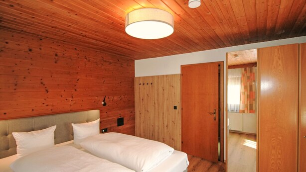 Une chambre à coucher aux murs lambrissés, avec un lit, une lampe de chevet et une armoire.