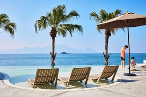 Un espace aménagé au bord de la piscine, avec des chaises longues, un palmier et une vue sur l’océan.