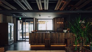 Un espace d’accueil avec un comptoir en bois, un petit tabouret et une grande plante en pot.