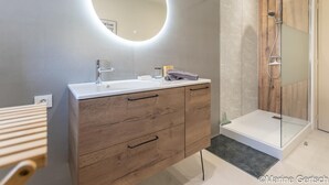 Un baño moderno con tocador de madera, espejo redondo, cabina de ducha de vidrio y lavabo blanco.