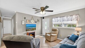 A living room with a fireplace, a ceiling fan, and a large window with a view. - Quiet Getaway Near Ft. Myers • Relax & Unwind (Alva)