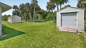 A residential area with a small shed, a fenced yard, and tall palm trees. - Quiet Getaway Near Ft. Myers • Relax & Unwind (Alva)