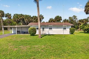 A single-story house with a covered porch, surrounded by a well-maintained lawn and palm trees. - Quiet Getaway Near Ft. Myers • Relax & Unwind (Alva)