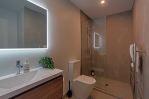 Une salle de bain moderne avec un grand miroir, une douche, des toilettes et un lavabo équipé de produits de toilette.