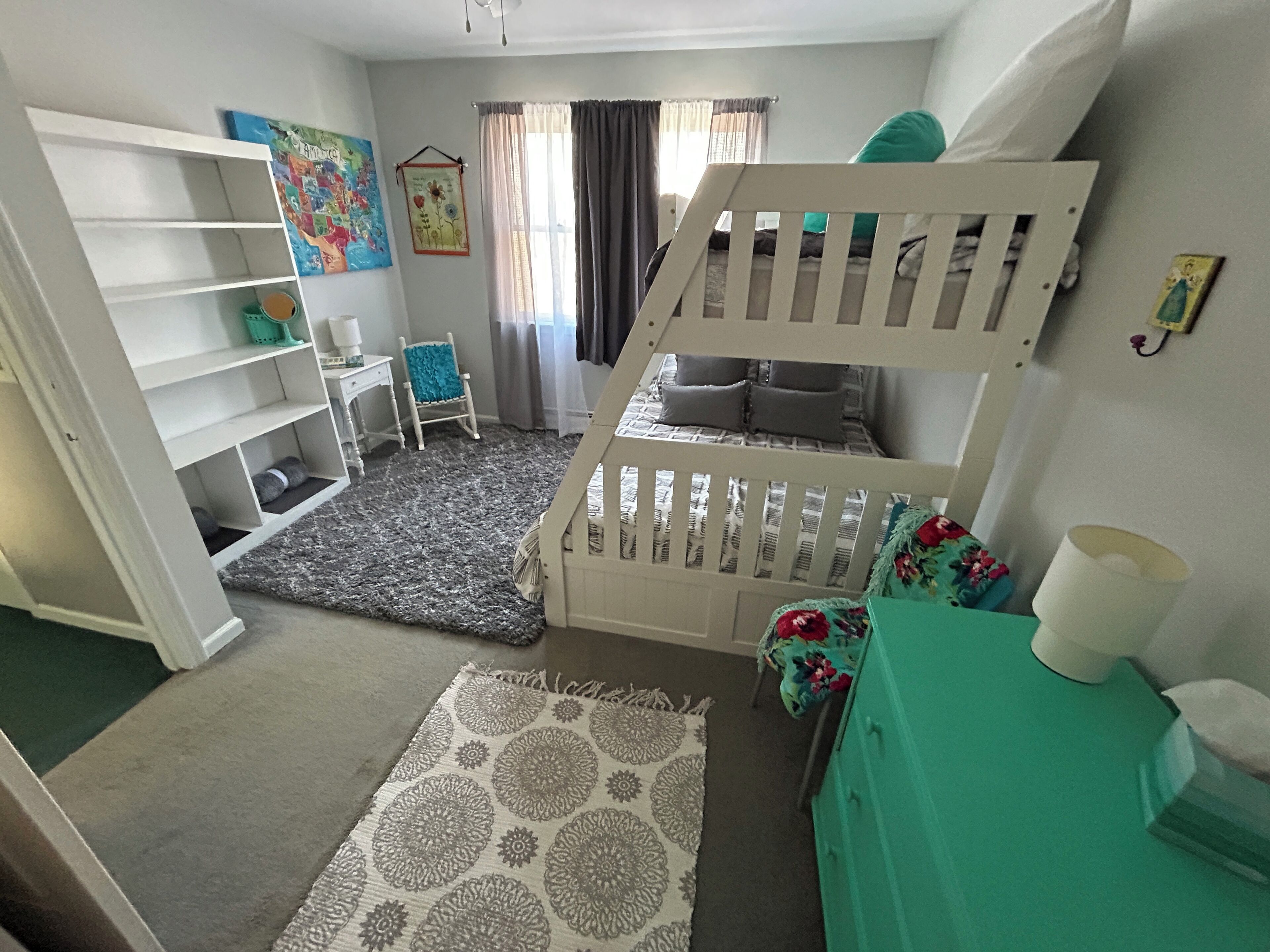 Une chambre d’enfant avec un lit superposé, un petit bureau, une chaise et une bibliothèque.