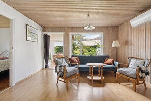 A room with a wooden ceiling, a sofa, two armchairs, a small round table, and a lamp.