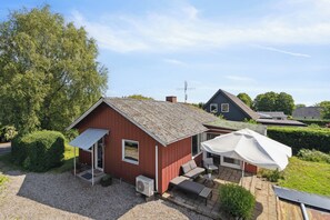 Punainen rakennus, jossa on kalteva katto, katettu terassi, jonka yläpuolella on valkoinen aurinkovarjo, ja sorapäällysteinen ajotie.