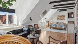 Une chambre de style « loft », avec un plafond en pente, un lit, un coin salon avec une table et une vue sur l’extérieur.