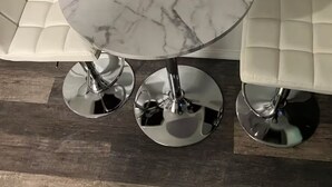 A round table with a marble top, flanked by two white cushioned chairs with chrome bases, set on a wooden floor. - CozyMiniStudio (Vancouver)