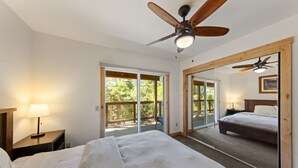 A bedroom with a bed, a nightstand, a ceiling fan, a large mirror, and a sliding glass door leading to an outdoor area.