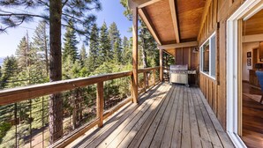 A wooden deck with a grill and a view of a forest.