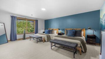 A bedroom with two beds, a window with curtains, a standing fan, and a nightstand with a lamp.
