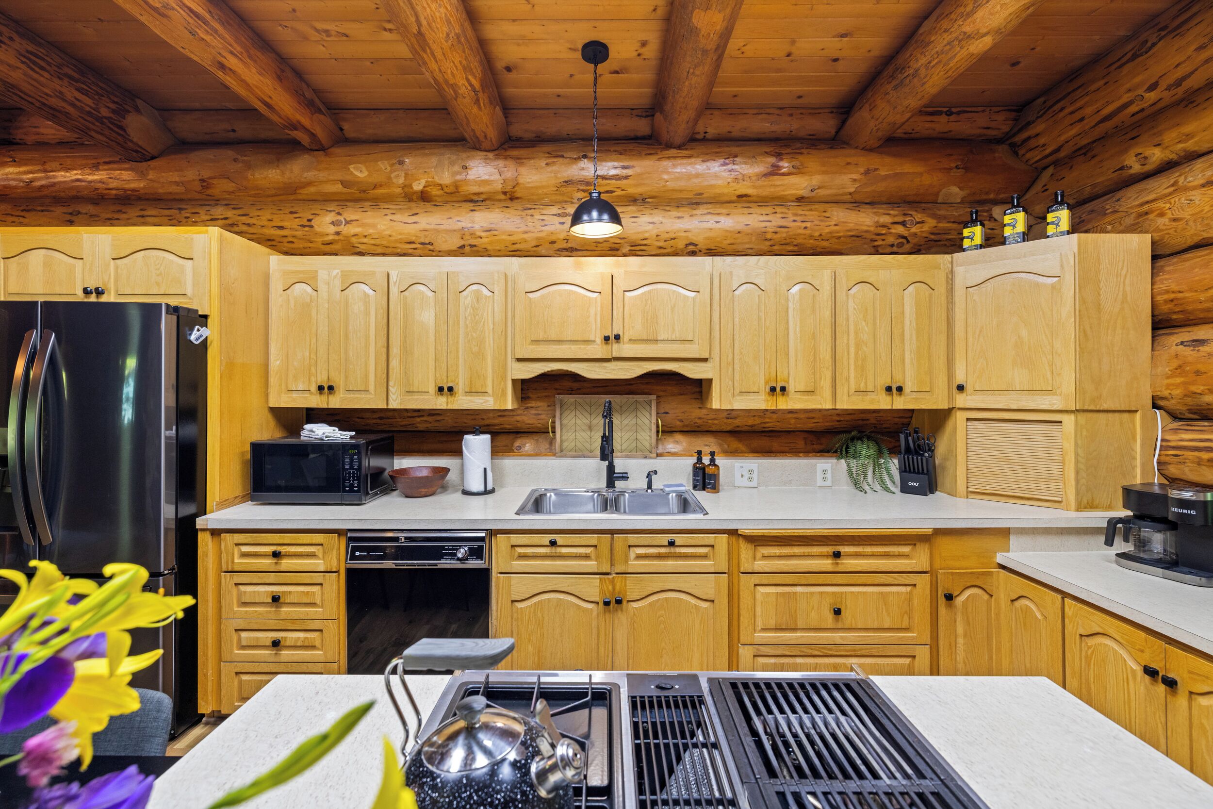 Una cocina con gabinetes de madera, un refrigerador de acero inoxidable, un microondas, un lavamanos y una estufa.