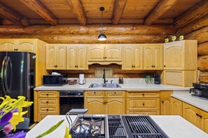 A kitchen with wooden cabinets, a stainless steel refrigerator, a microwave, a sink, and a stove. - American Alps Lodge: Riverfront, Beach, Hot Tub, EV Charger, Game Room (Marblemount)