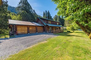 A log cabin with a gravel driveway and a fenced yard. - American Alps Lodge: Riverfront, Beach, Hot Tub, EV Charger, Game Room (Marblemount)