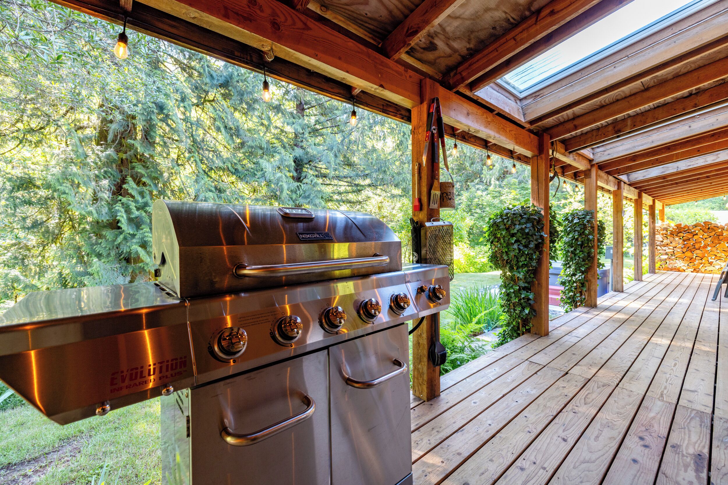 Zona de parrilla al aire libre con una parrilla de acero inoxidable, cubierta de madera y follaje circundante.