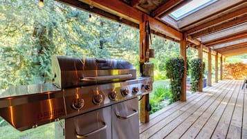 Zona de parrilla al aire libre con una parrilla de acero inoxidable, cubierta de madera y follaje circundante.