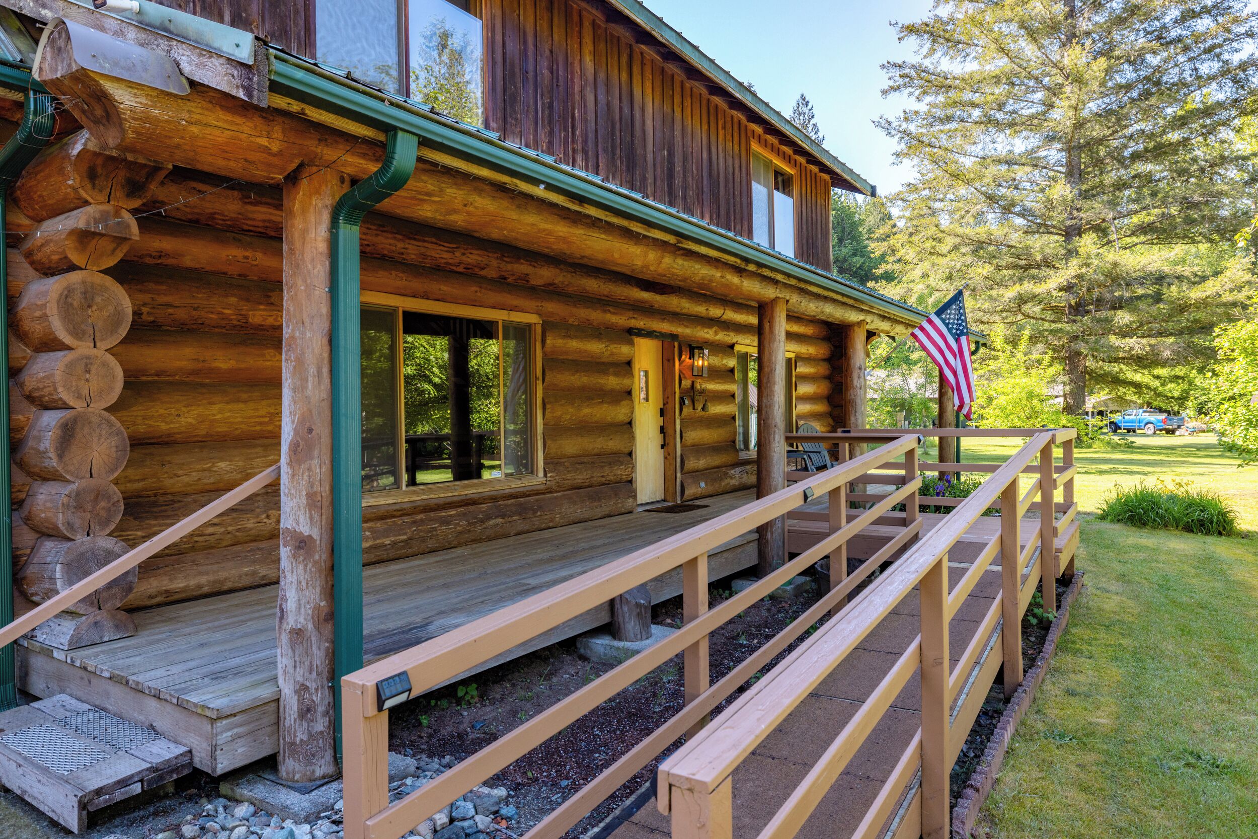 A log cabin with a porch, a flag, and a view of the surrounding forest.