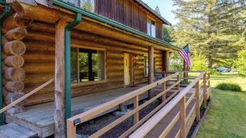 A log cabin with a porch, a flag, and a view of the surrounding forest.