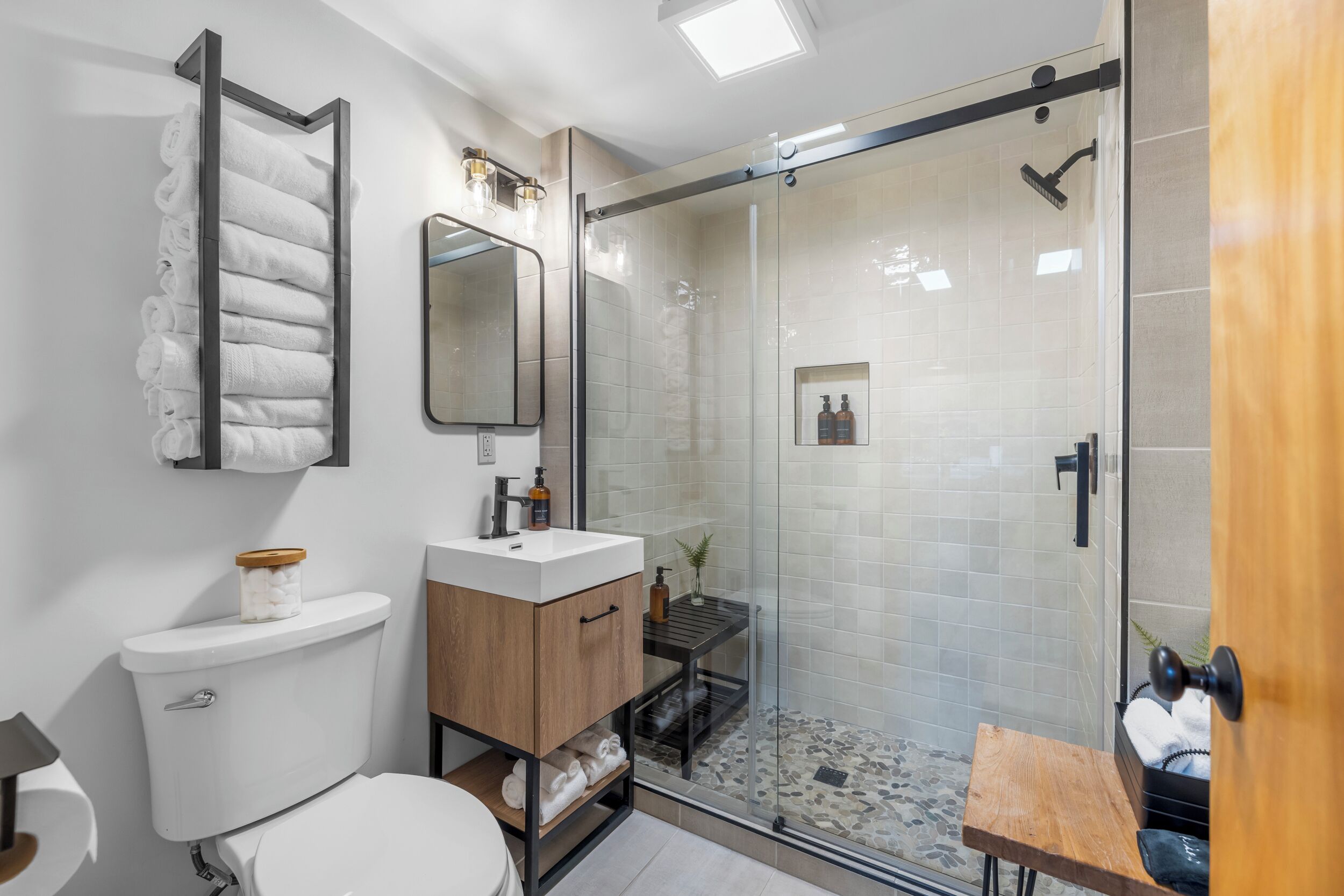 A modern bathroom with a glass-enclosed shower, a toilet, a sink with a wooden cabinet, and a towel rack.