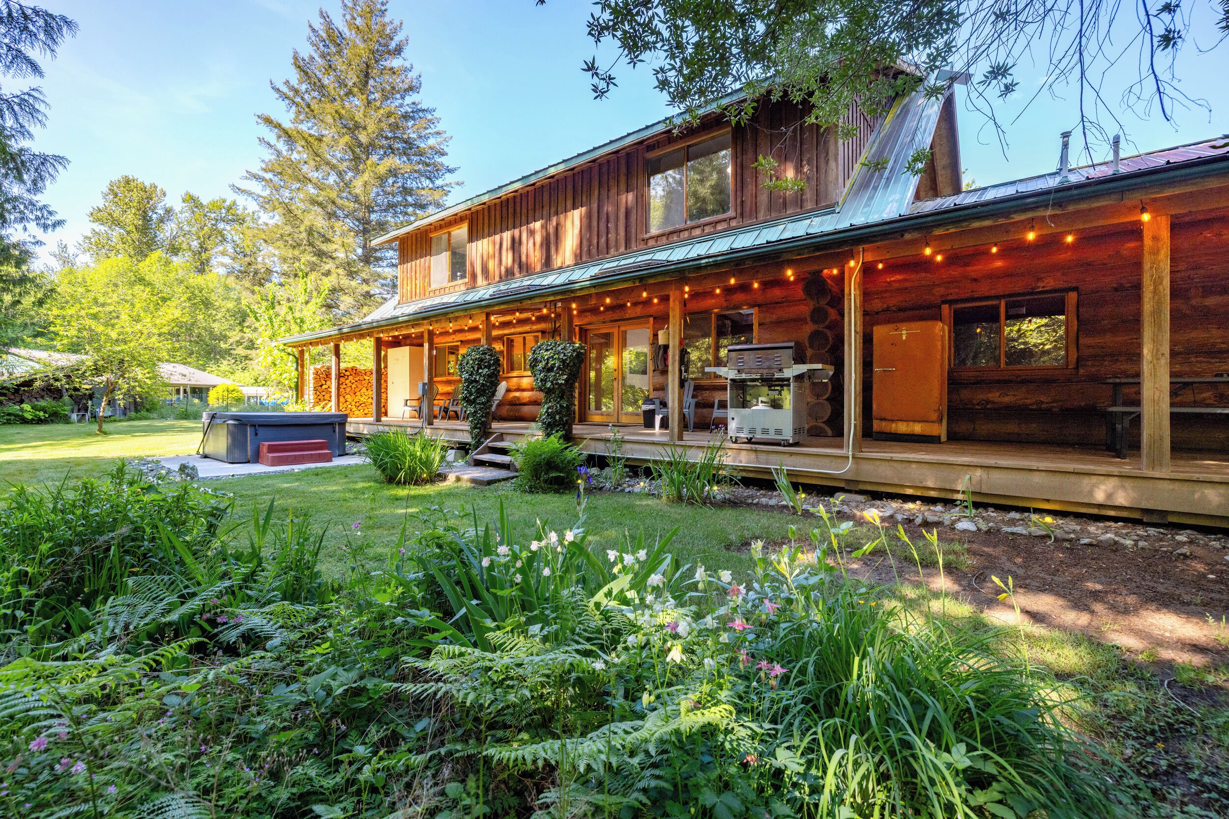 A wooden cabin with a covered porch, a barbecue grill, and a garden with various plants and flowers.