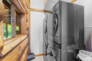 Un lavadero pequeño con lavadora y secadora de acero inoxidable, paredes de madera y una ventana con persianas.